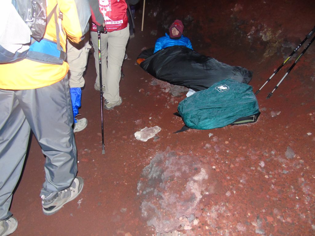 People hiking the trail a person laying down resting on the side. Whilst Climbing Mt. Fuji at night.