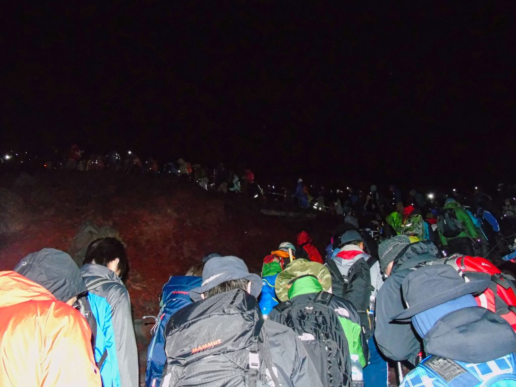 A trail of people following the path up to the summit whilst climbing Mt. Fuji at night.