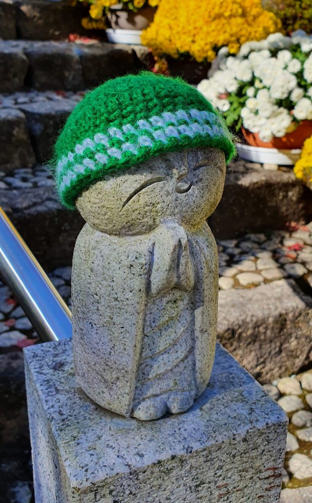 A small statue of a Buddhist priest wearing a green wool knitted hat at Hotokuji Temple Gunma's Hidden Gem